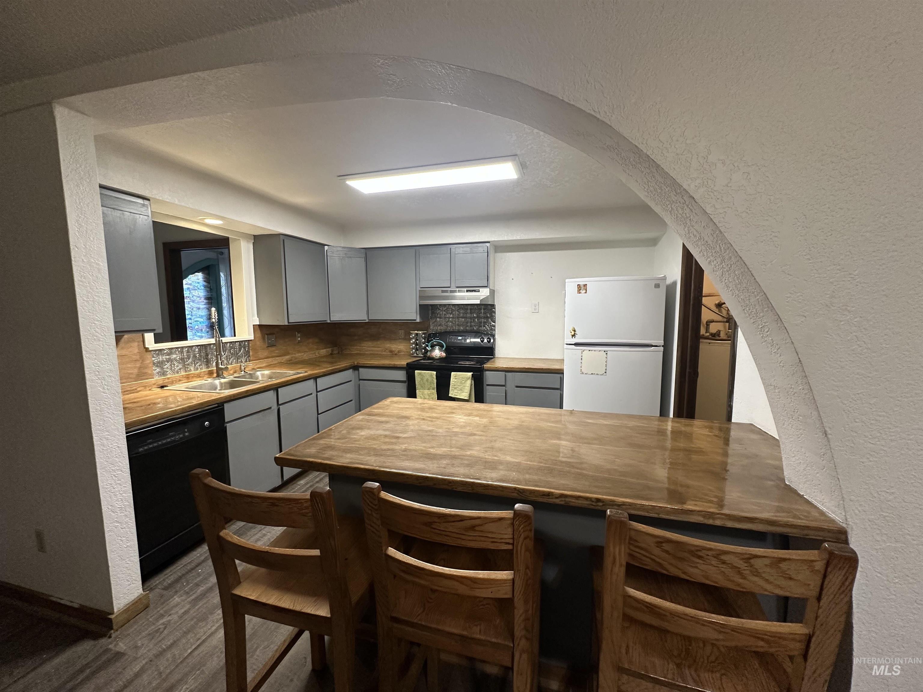 5860 Akron Road New Plymouth, ID 83655 - Photo 7 of 33 Kitchen featuring a textured wall, gray cabinetry, arched walkways, black appliances, and backsplash