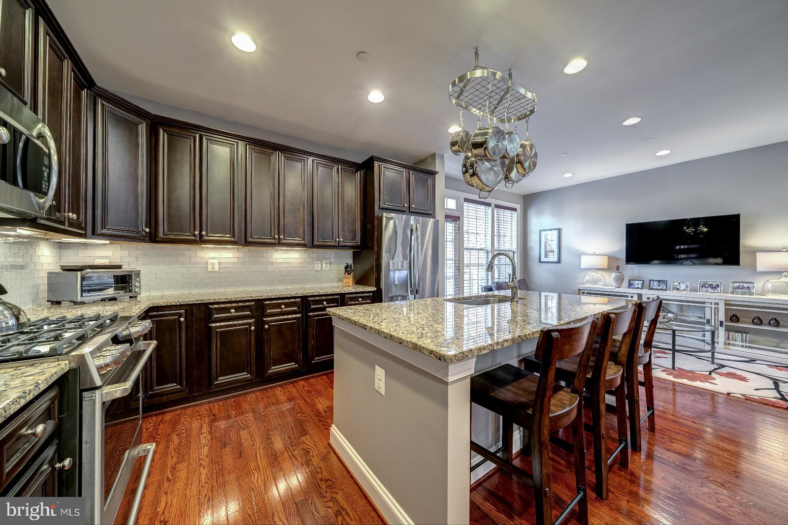 a kitchen with stainless steel appliances granite countertop a stove top oven a sink dishwasher a dining table and chairs with wooden floor