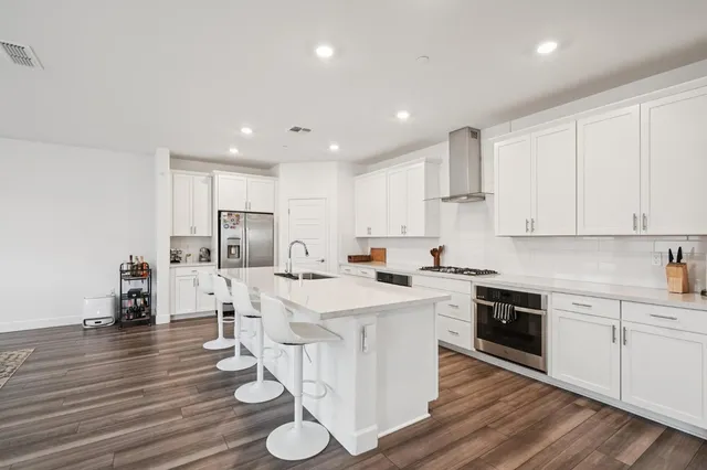 a kitchen with stainless steel appliances granite countertop a stove a sink a refrigerator and white cabinets with wooden floor