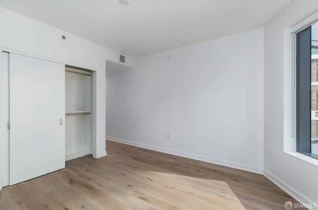 a view of an empty room with wooden floor and closet