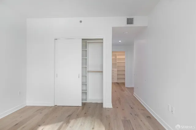 a view of an empty room with wooden floor and closet
