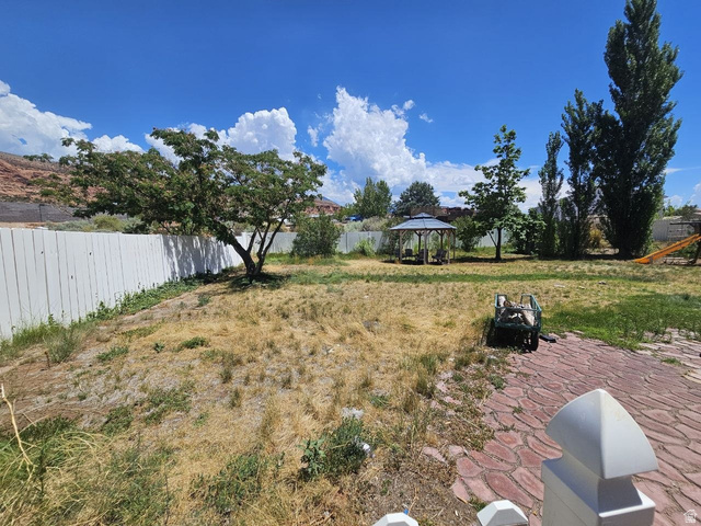 52 Quail Court Moab, UT 84532 - Photo 19 of 36 Spacious backyard featuring a white privacy fence, mature trees, a metal gazebo, and a red paver patio