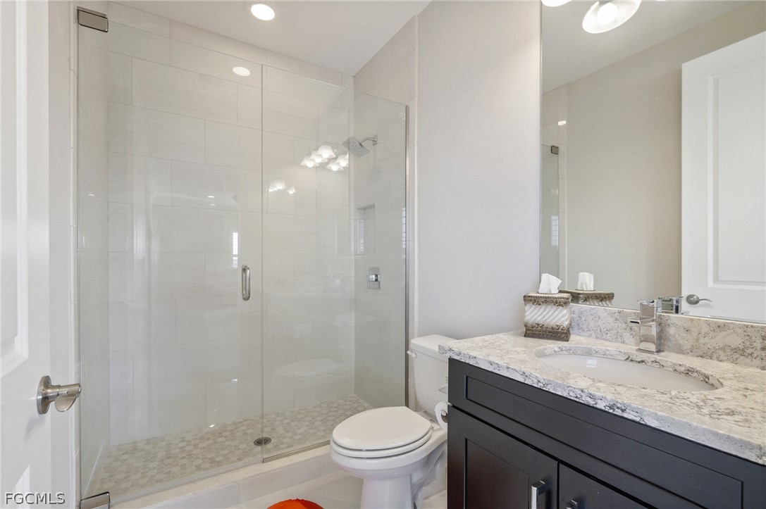 9345 Tulipano Terrace Naples, FL 34119 - Photo 31 of 50 a bathroom with a granite countertop sink a toilet a mirror and shower