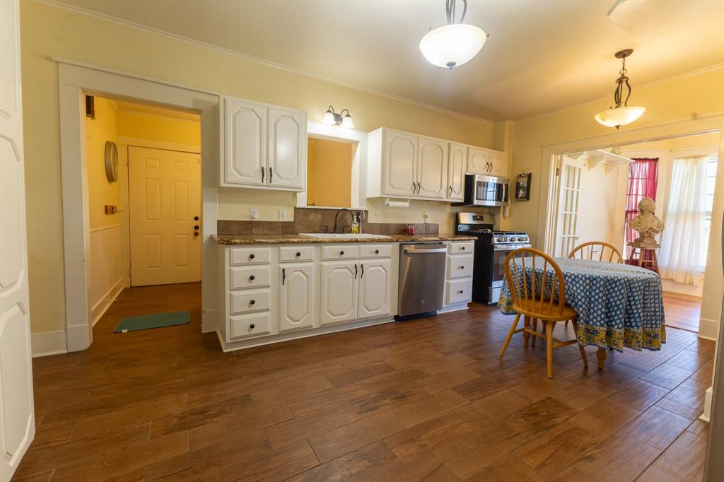 1115 Austin Street Coleman, TX 76834 - Photo 8 of 40 a kitchen with stainless steel appliances granite countertop a stove top oven a sink a dining table and chairs with wooden floor