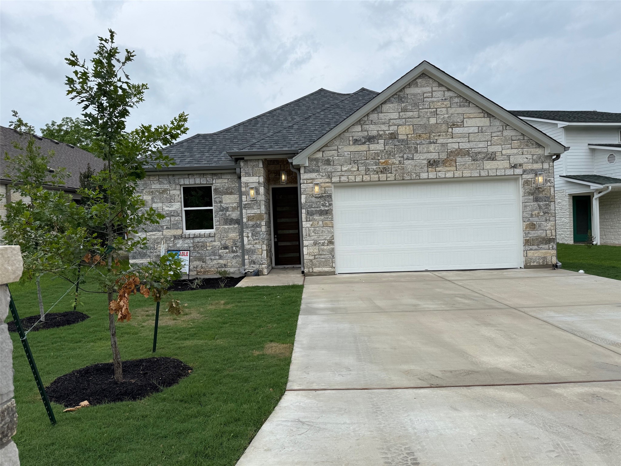 Stone facade home with an attached garage, paved driveway, and manicured lawn