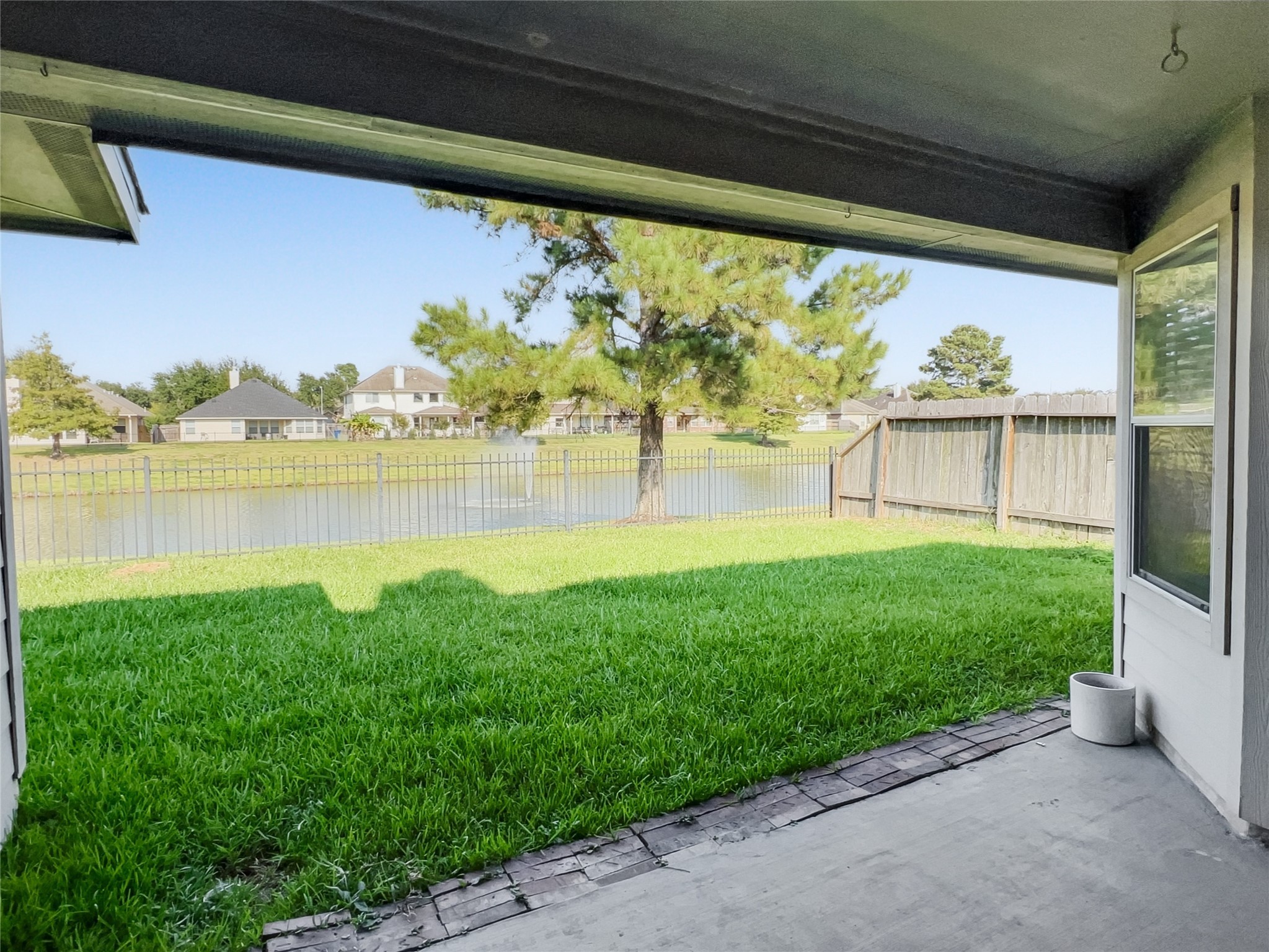 20326 Linshire Drive Spring, TX 77388 - Photo 22 of 24 This photo showcases a covered patio with a view of a lush green backyard, bordered by a fence overlooking a serene pond. Ideal for enjoying outdoor relaxation and picturesque water views.