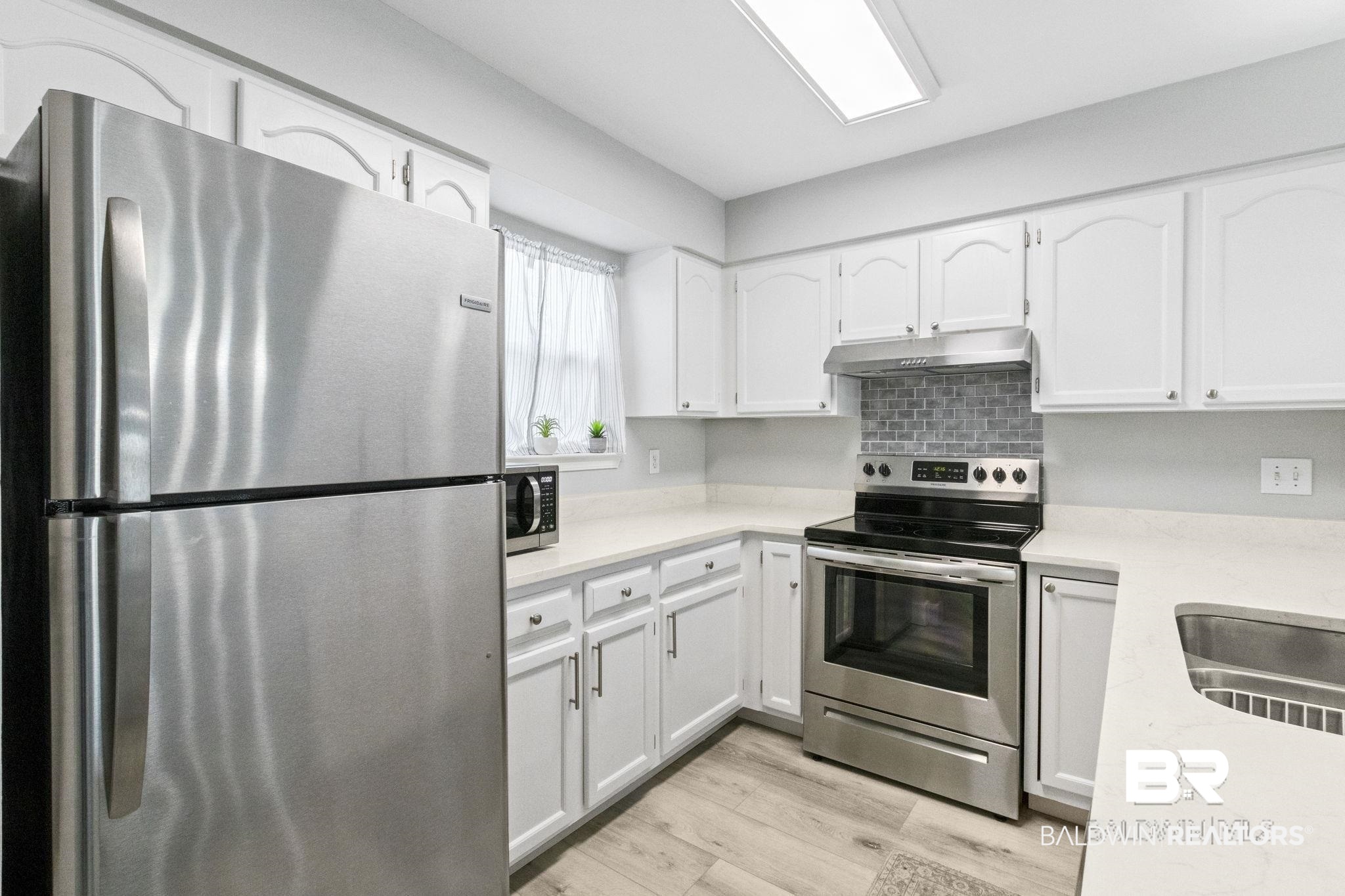 25861 Canal Road, Unit 77 Orange Beach, AL 36561 - Photo 19 of 48 Kitchen featuring appliances with stainless steel finishes, white cabinets, light wood-style flooring, under cabinet range hood, and light stone counters