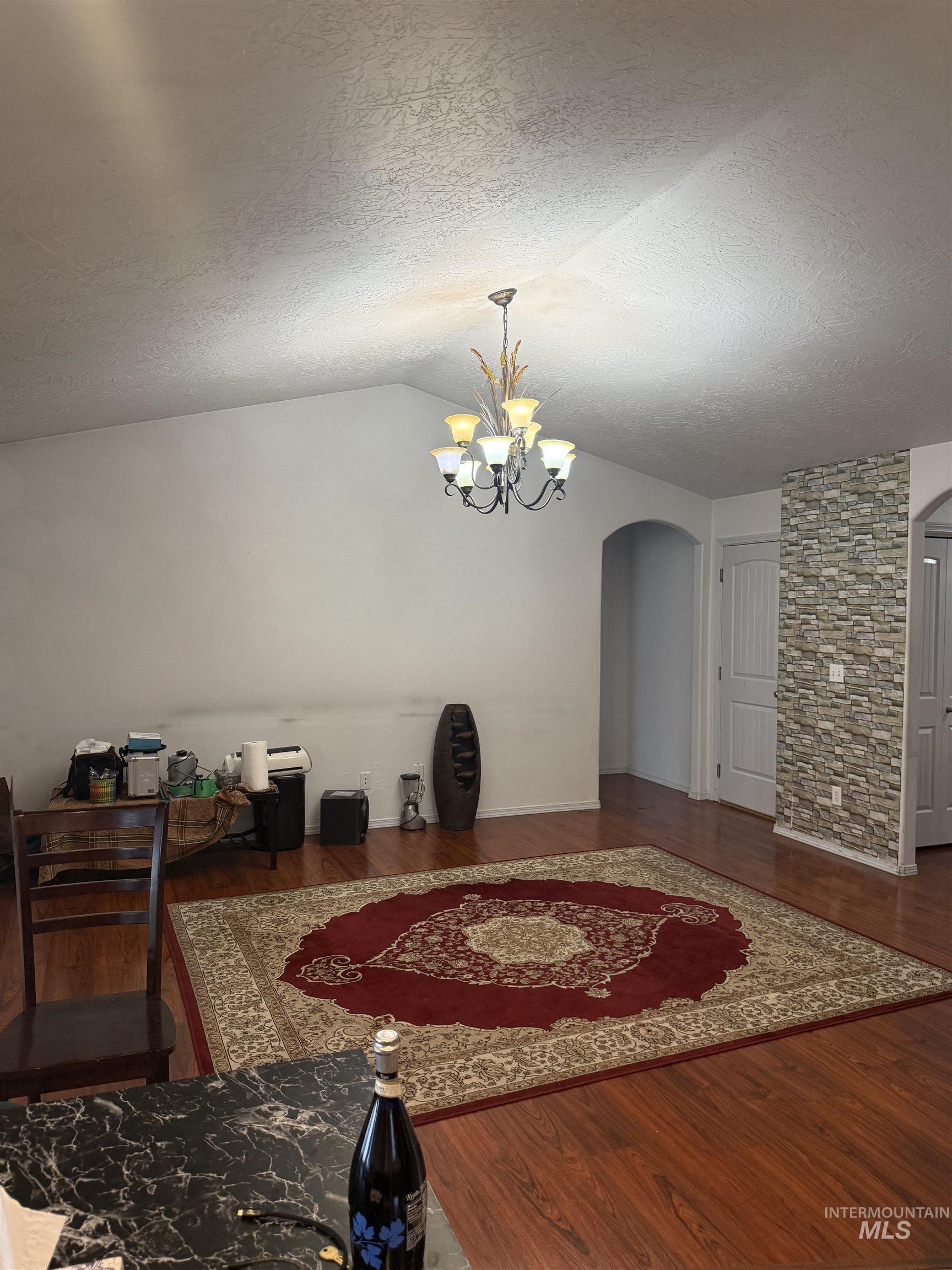 494 Adria Lane Twin Falls, ID 83301 - Photo 10 of 19 Dining room featuring arched walkways, a textured ceiling, vaulted ceiling, dark wood-style flooring, and a chandelier