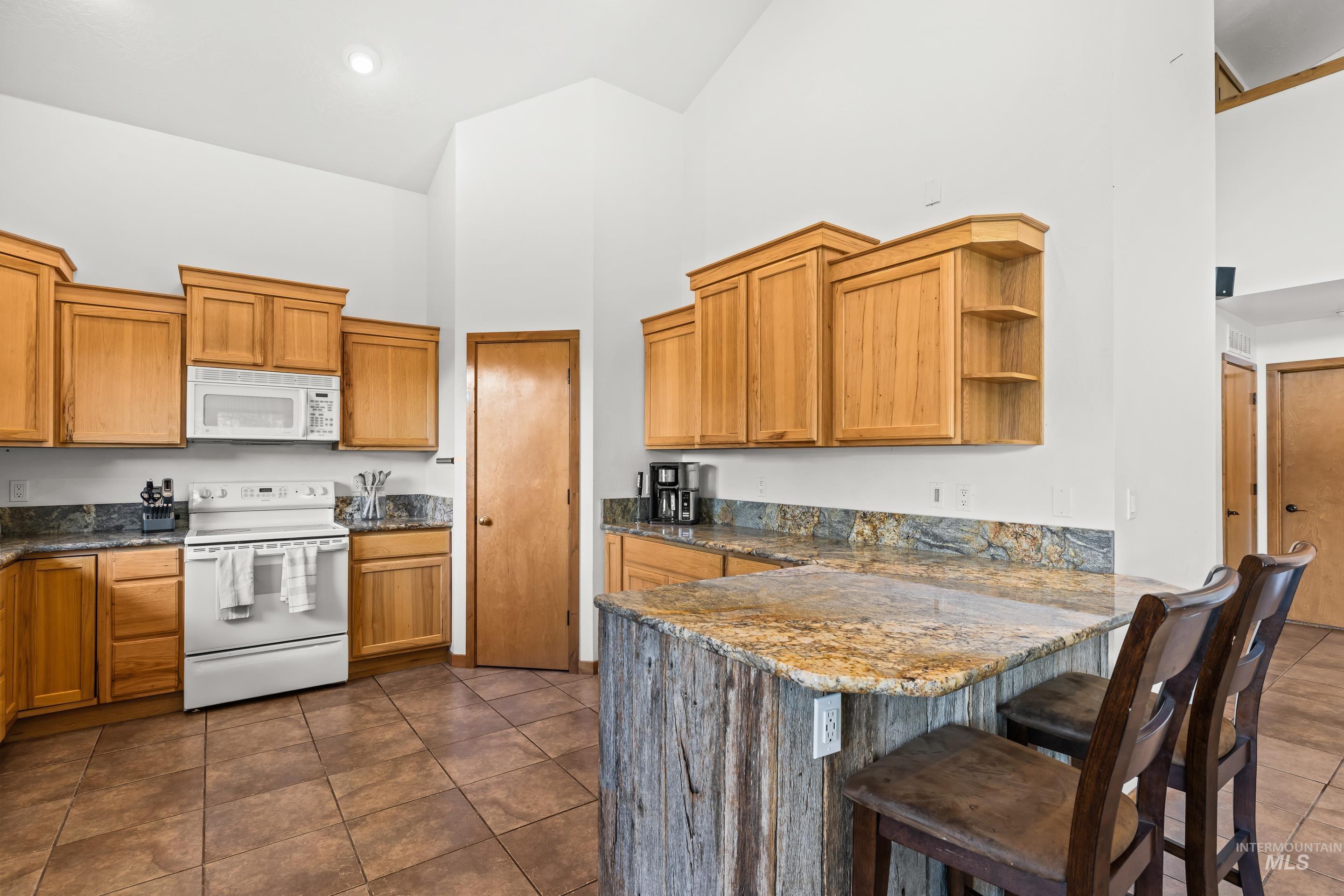 92 Cruickshank Road Horseshoe Bend, ID 83629 - Photo 18 of 50 Kitchen featuring wood cabinetry, stone countertops, white appliances, a breakfast bar with a wood-finish base, and tile flooring