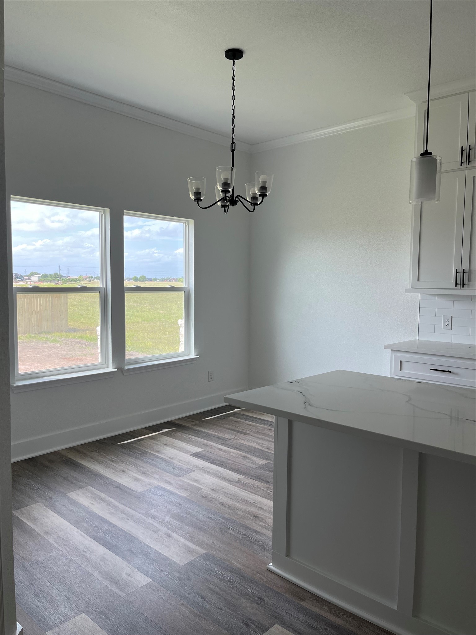 33416 FM 521 Road Angleton, TX 77515 - Photo 10 of 21 This photo showcases a bright dining area with large windows offering a view of the outdoors. The room features a modern light fixture, medium gray/wood water proof plank flooring, and a sleek kitchen island with Quartz countertops.