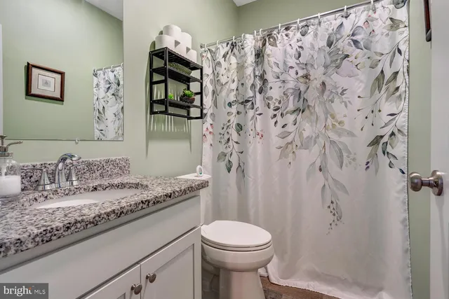 a bathroom with a granite countertop sink a toilet and shower curtain