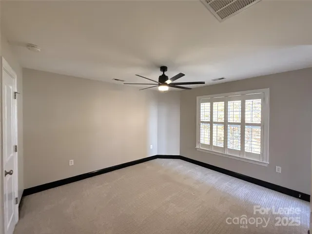 an empty room with chandelier fan and windows