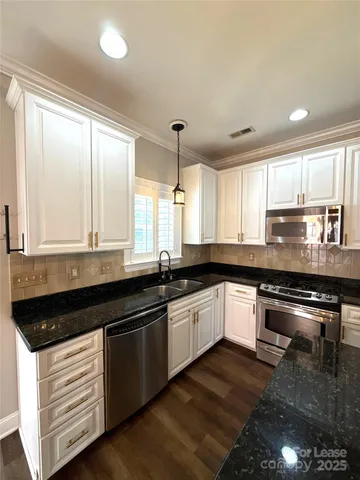 a kitchen with stainless steel appliances granite countertop a stove a sink and white cabinets