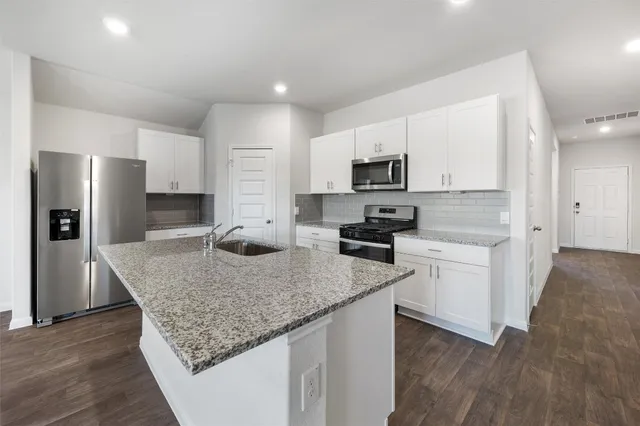 a kitchen with kitchen island granite countertop a stove top oven a sink dishwasher a refrigerator and white cabinets with wooden floor