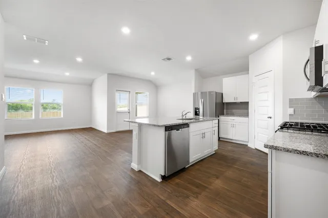 a large kitchen with stainless steel appliances granite countertop a large stove a sink a refrigerator white cabinets and wooden floor next to a large window