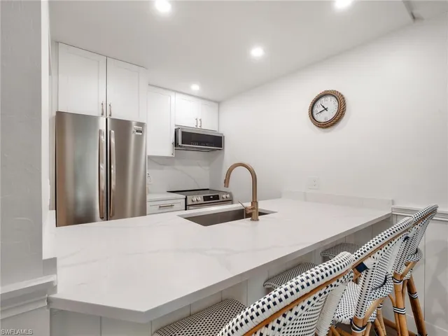 a kitchen with stainless steel appliances a sink a stove a refrigerator with white cabinets and wooden floor