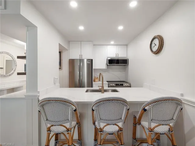 a kitchen with stainless steel appliances granite countertop a dining table chairs refrigerator and microwave