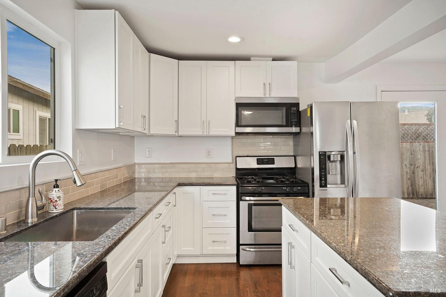 a kitchen with granite countertop a sink white cabinets and stainless steel appliances