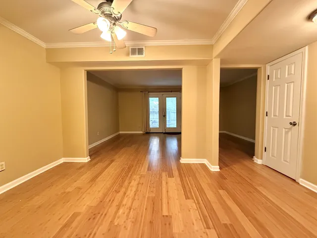 a view of an empty room with wooden floor and a ceiling fan