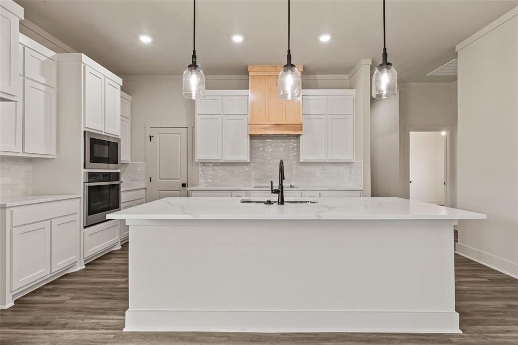 138 Dana Pt Road Lorena, TX 76655 - Photo 9 of 24 Kitchen island featuring a white countertop with a built-in sink and matte black faucet, complemented by three pendant lights
