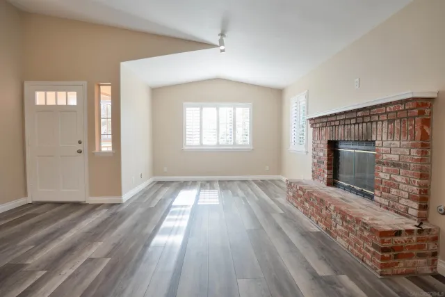 a view of an empty room with wooden floor fireplace and a window