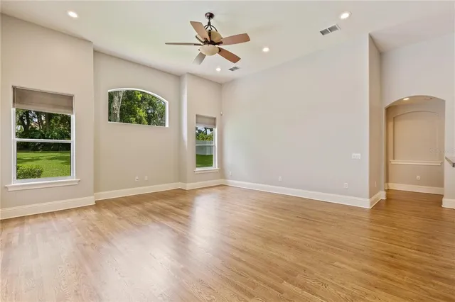 an empty room with wooden floor a ceiling fan and windows