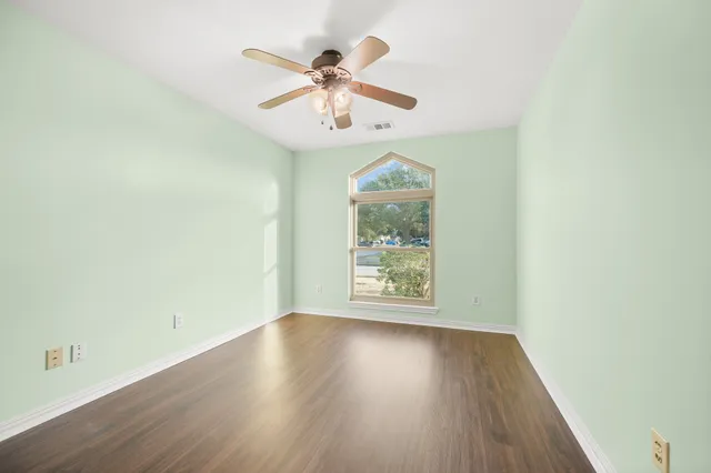 an empty room with wooden floor chandelier fan and windows