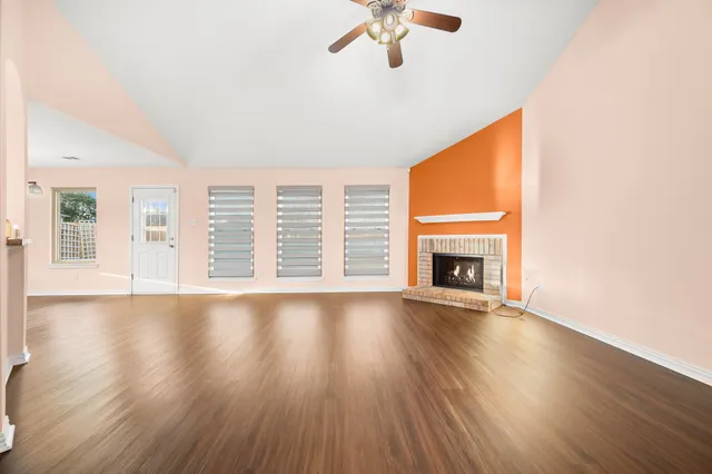 an empty room with wooden floor fan and windows