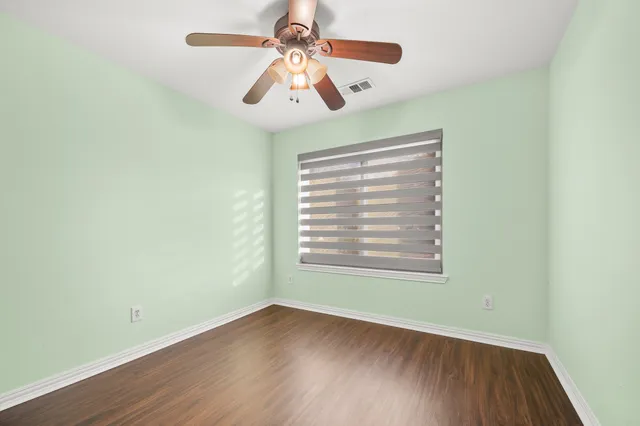 an empty room with wooden floor chandelier fan and windows