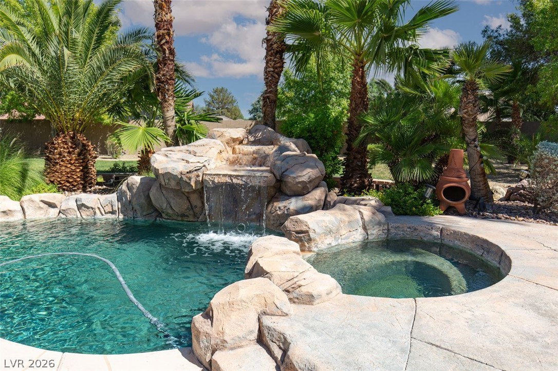 4670 Los Rancheros Avenue Las Vegas, NV 89129 - Photo 40 of 57 A stone waterfall cascades into a sparkling swimming pool flanked by palm trees.