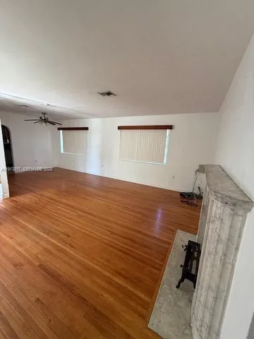 an empty room with wooden floor fan and windows