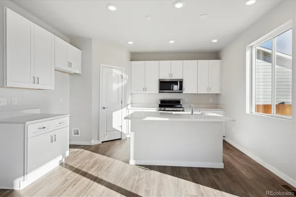 a kitchen with stainless steel appliances a stove top oven a sink a refrigerator white cabinets and wooden floor