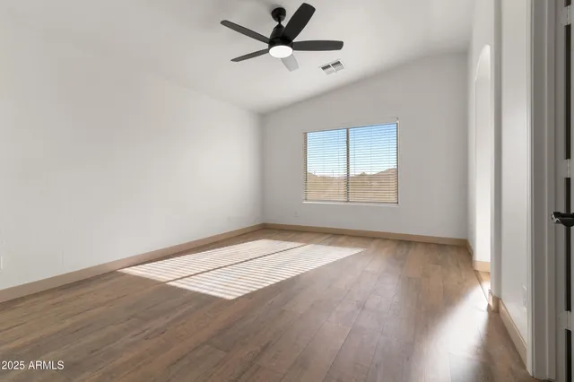 an empty room with wooden floor fan and windows