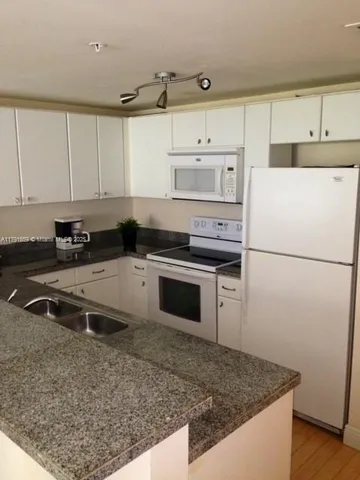 a kitchen with granite countertop a refrigerator sink stove and white cabinets