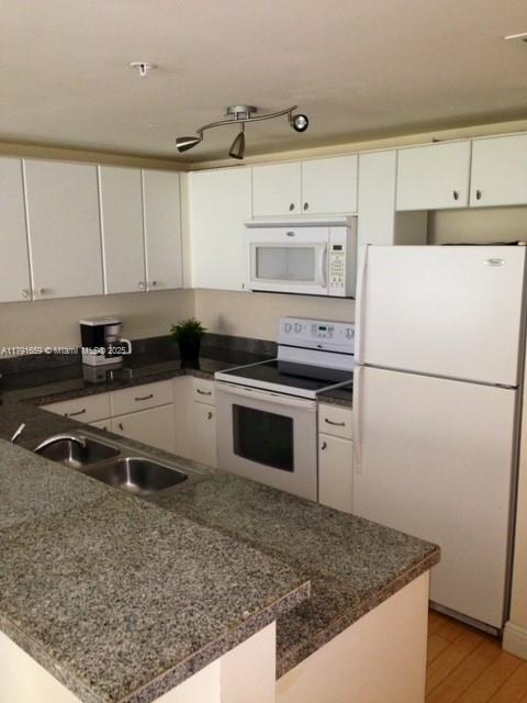 2740 Southwest 28th Terrace, Unit 304 Miami, FL 33133 - Photo 10 of 13 a kitchen with granite countertop a refrigerator sink stove and white cabinets