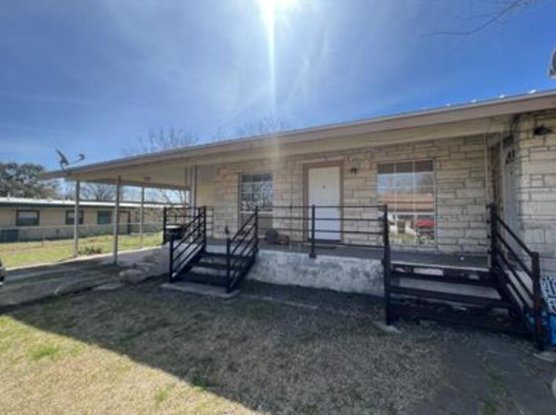 View of front facade featuring covered porch, stone siding, and a front lawn