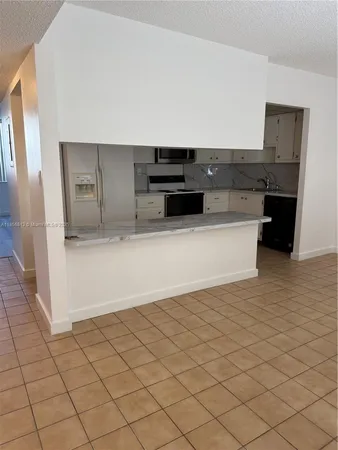 a view of a refrigerator in kitchen and an empty room