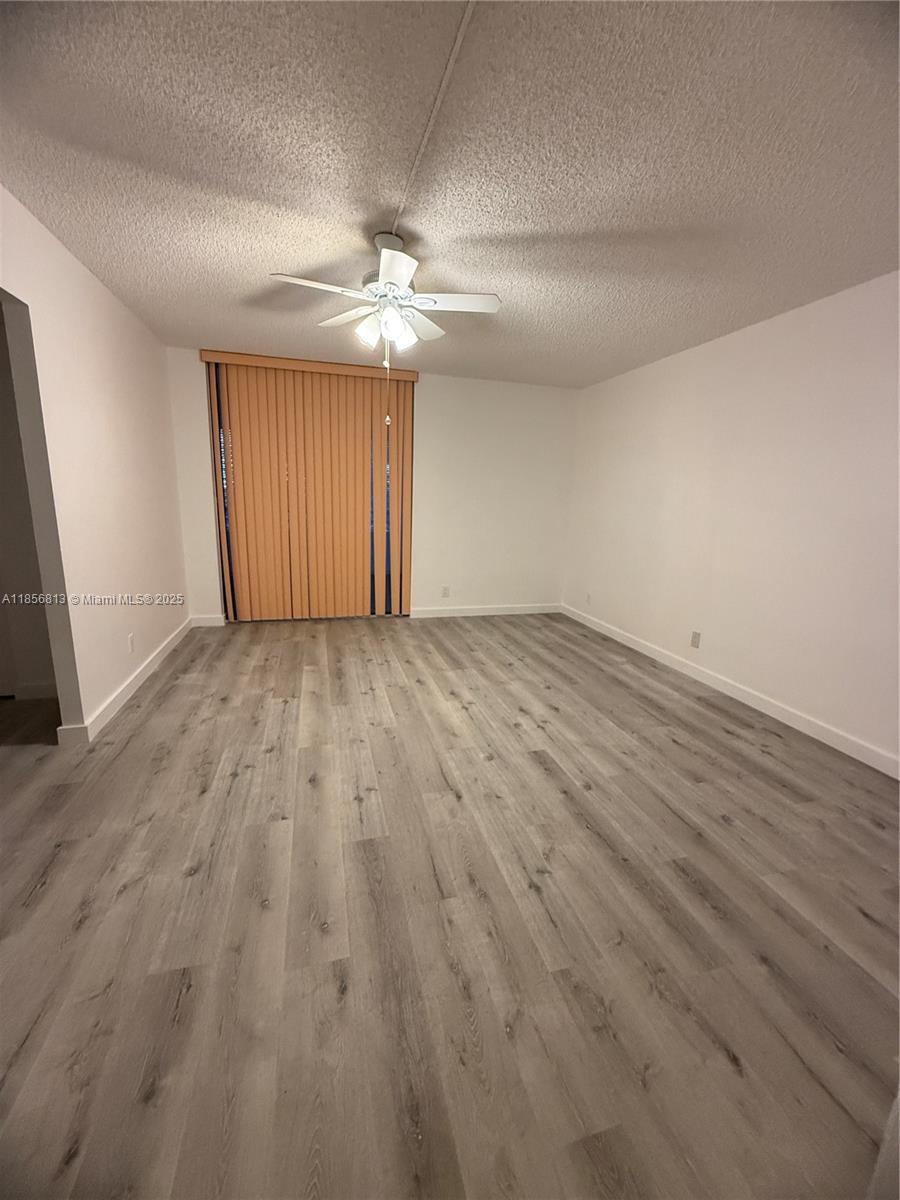 20441 Northeast 30th Avenue, Unit 1129 Aventura, FL 33180 - Photo 8 of 16 an empty room with wooden floor ceiling fan and windows