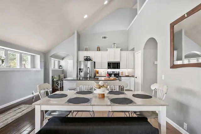 a kitchen with stainless steel appliances a refrigerator a stove a sink dishwasher a dining table and chairs with wooden floor