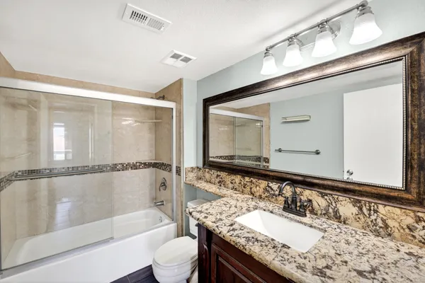a bathroom with a granite countertop bathtub shower sink vanity and toilet