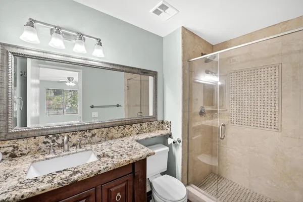 a bathroom with a granite countertop sink vanity mirror shower and toilet