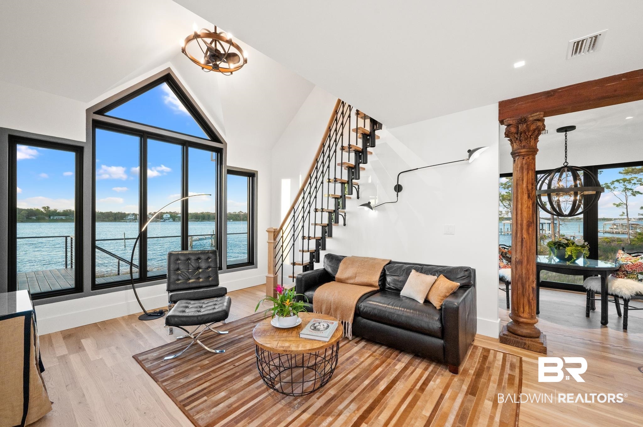 33349 River Road Orange Beach, AL 36561 - Photo 4 of 61 Spacious living area featuring expansive windows with water scenery, soaring vaulted ceilings, wood-finish flooring, a contemporary open-tread staircase with metal balusters, and a decorative wooden column