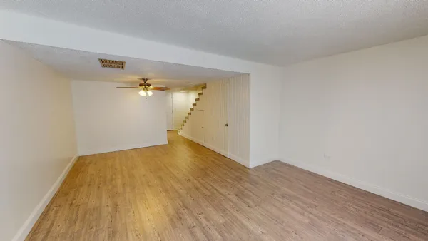 a view of empty room with wooden floor and fan