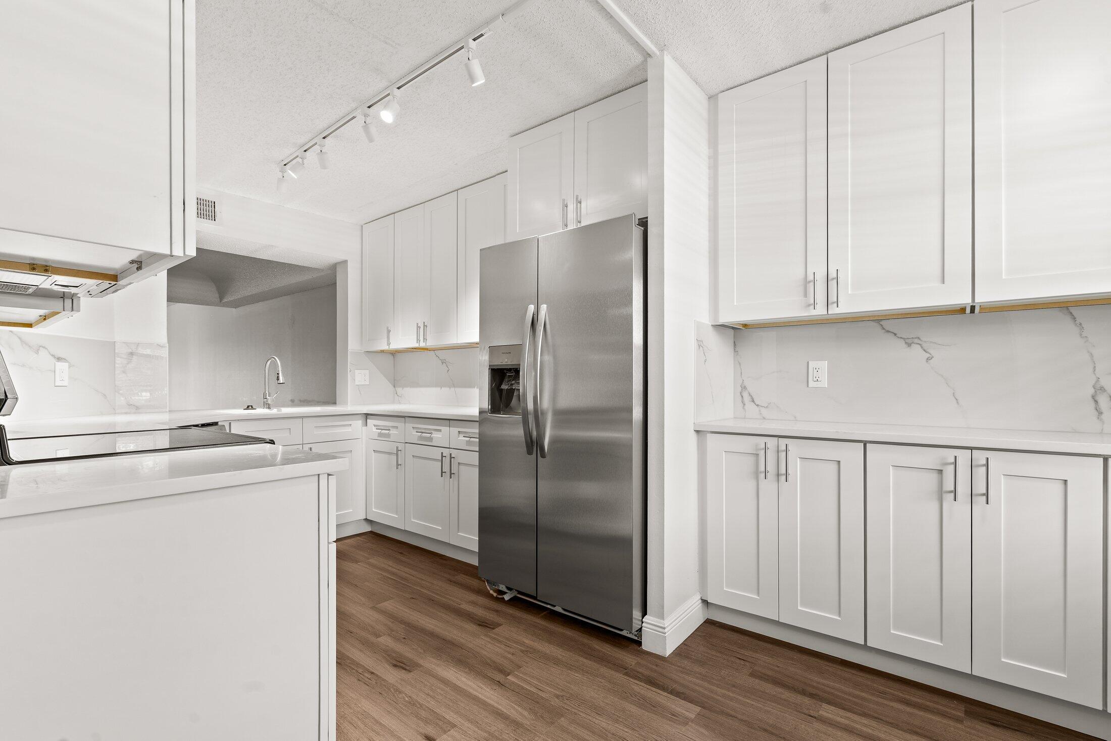 23395 Carolwood Lane, Unit 207 Boca Raton, FL 33428 - Photo 7 of 39 a kitchen with stainless steel appliances granite countertop a refrigerator a sink and white cabinets with wooden floor