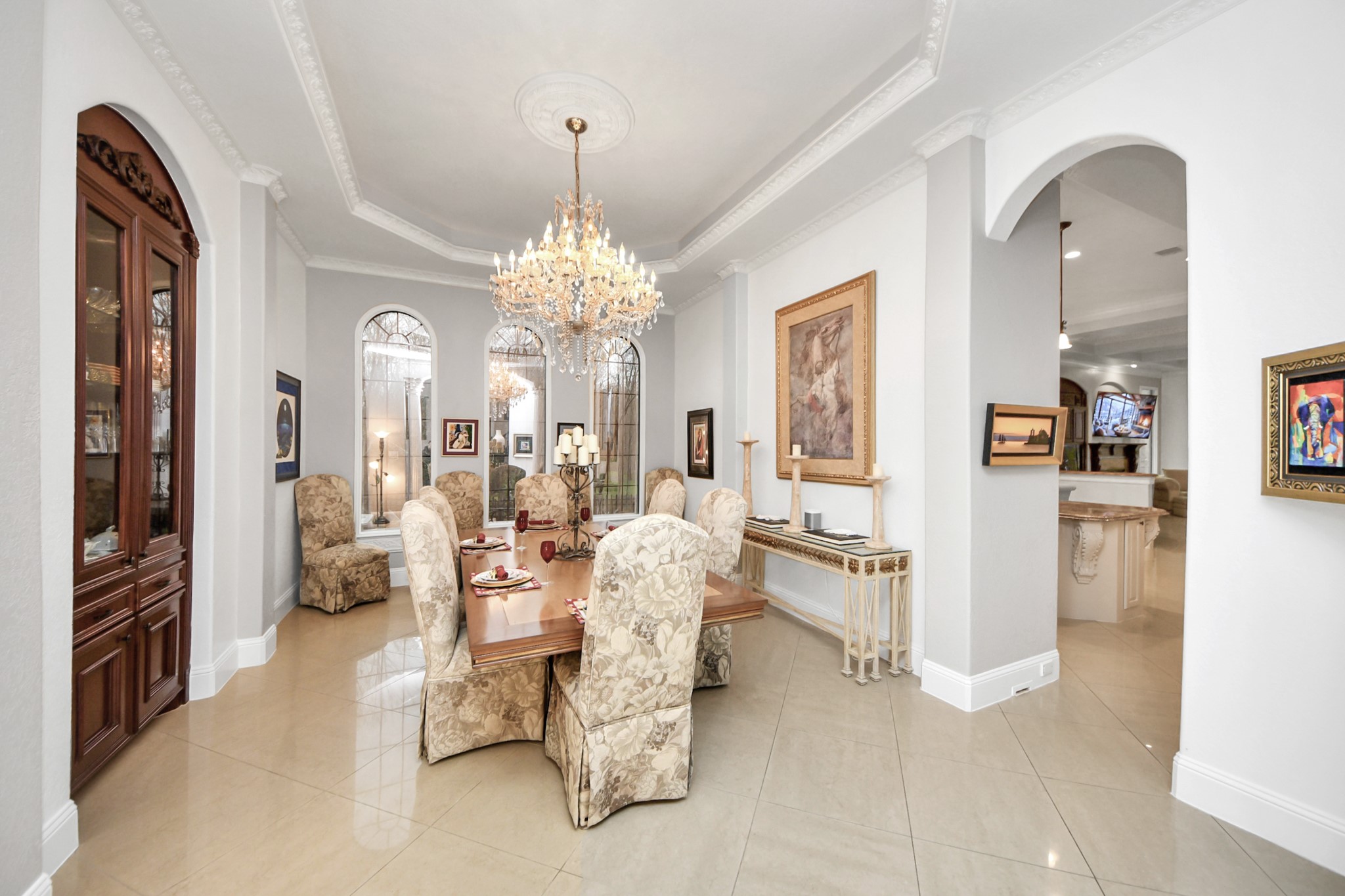 11503 Renaissance Drive Montgomery, TX 77356 - Photo 8 of 50 This elegant formal dining room makes a striking first impression with soaring ceilings, intricate crown molding, and a dazzling crystal chandelier that anchors the space. Tall arched windows flood the room with natural light, creating a bright and airy atmosphere ideal for both intimate dinners and large gatherings. The thoughtfully designed layout comfortably accommodates a generous dining table, while classic architectural details and curated wall art add timeless sophistication.