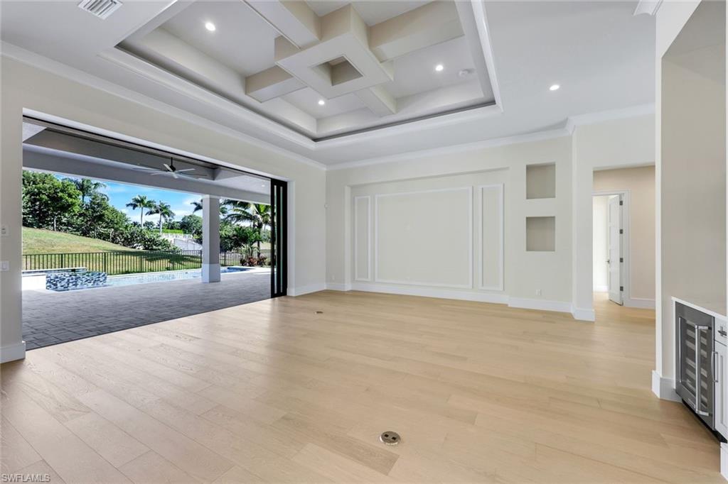 14282 Charthouse Circle Naples, FL 34114 - Photo 12 of 48 Empty room with coffered ceiling, beam ceiling, beverage cooler, light wood-type flooring, and ornamental molding