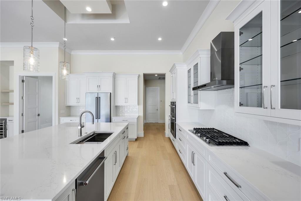 14282 Charthouse Circle Naples, FL 34114 - Photo 15 of 48 Kitchen with backsplash, ornamental molding, light stone counters, pendant lighting, and white cabinetry
