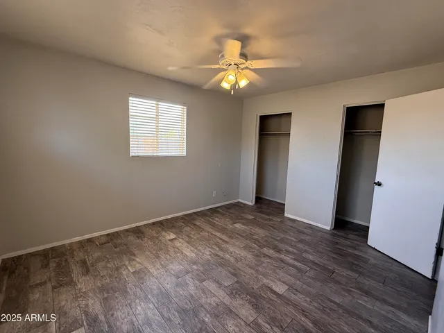 an empty room with wooden floor chandelier fan and windows