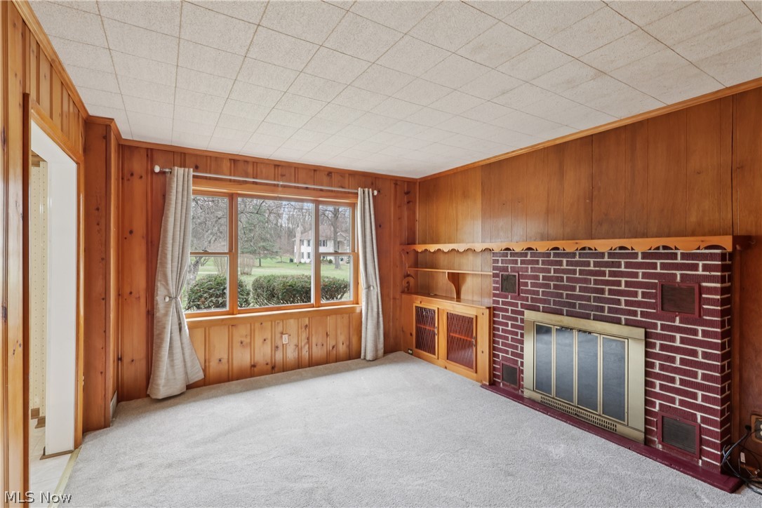 402 Yager Road Clinton, OH 44216 - Photo 8 of 38 Living room with large picture window, brick fireplace, Knotty Pine walls, built-ins, and carpet flooring