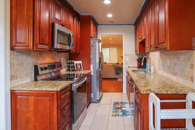 a kitchen with stainless steel appliances granite countertop wooden cabinets a stove top oven a granite counter top and a view of living room